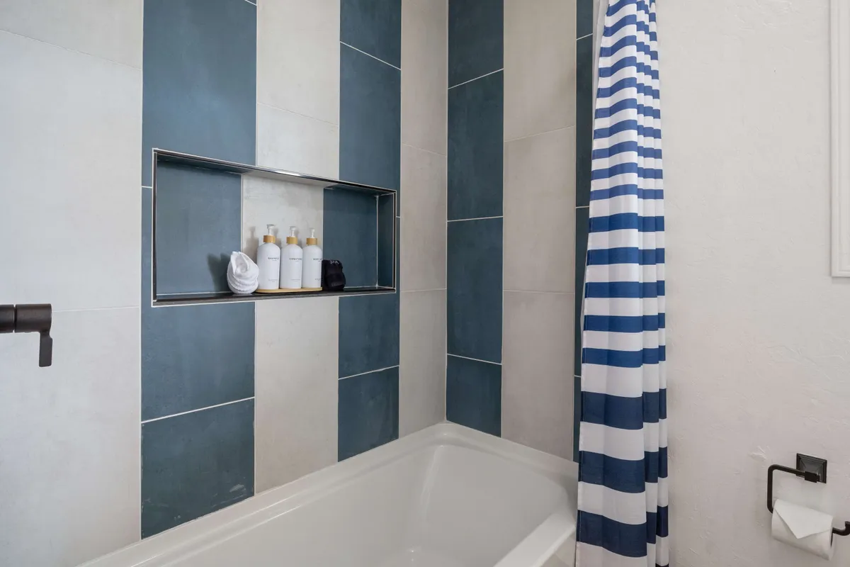 A serene bathroom with a striped shower curtain, shelf stocked with toiletries, and a calming blue and white color scheme. The space feels fresh and inviting, perfect for unwinding after a busy day.