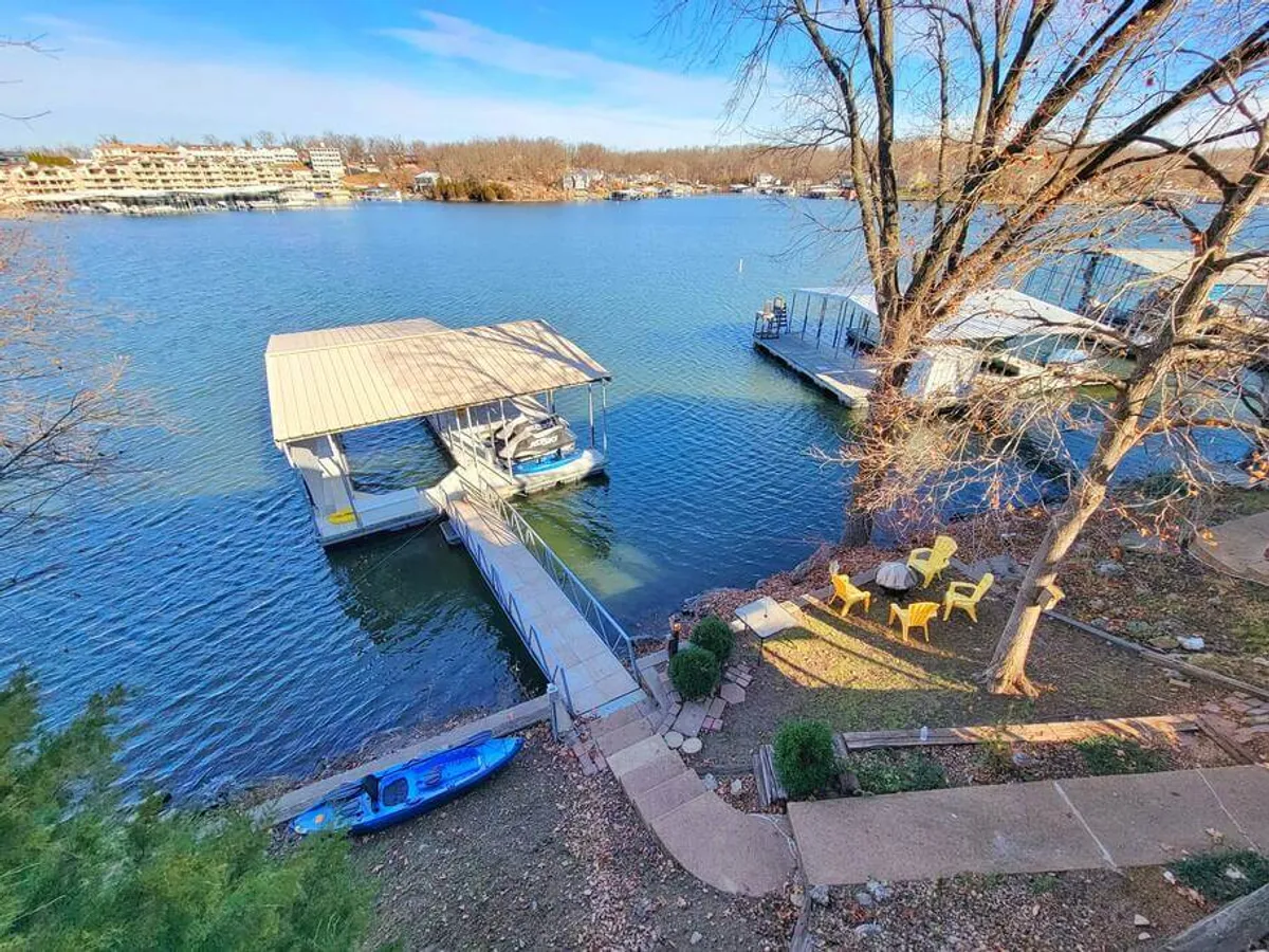 A private dock extends over calm water, featuring a boat lift, vibrant yellow chairs, a kayak along the dock, and a lush treeline in the background. The setting feels secluded and peaceful, with the dock directly accessible for fishing, relaxing, or launching a kayak. The presence of comfortable seating encourages moments of lakeside leisure.