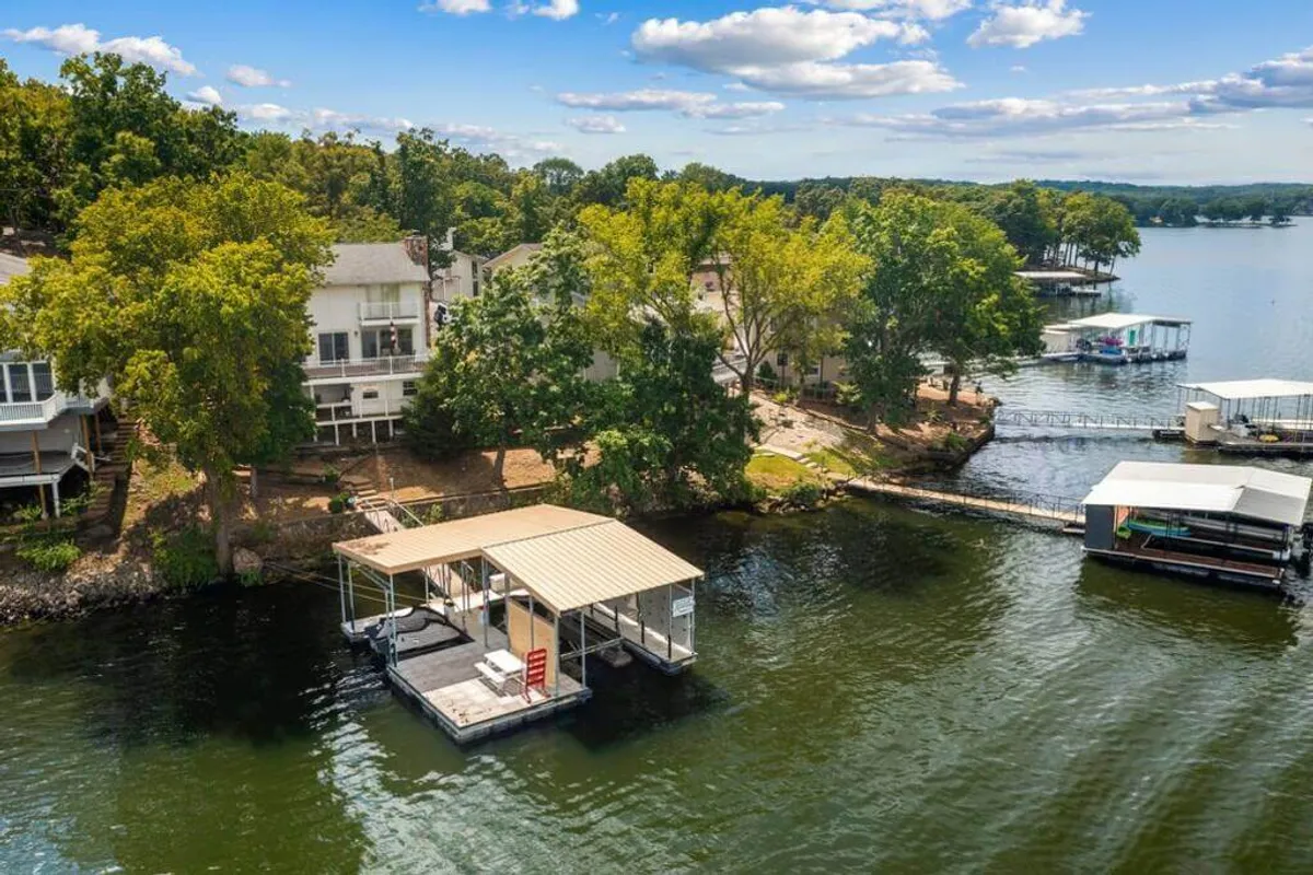 This image features a waterfront dock surrounded by lush trees and neighboring lake houses. The dock is an inviting spot for sunbathing, gathering with friends, or starting a water adventure. The water’s edge and scenic lake views evoke a sense of relaxation and fun, perfect for group activities.