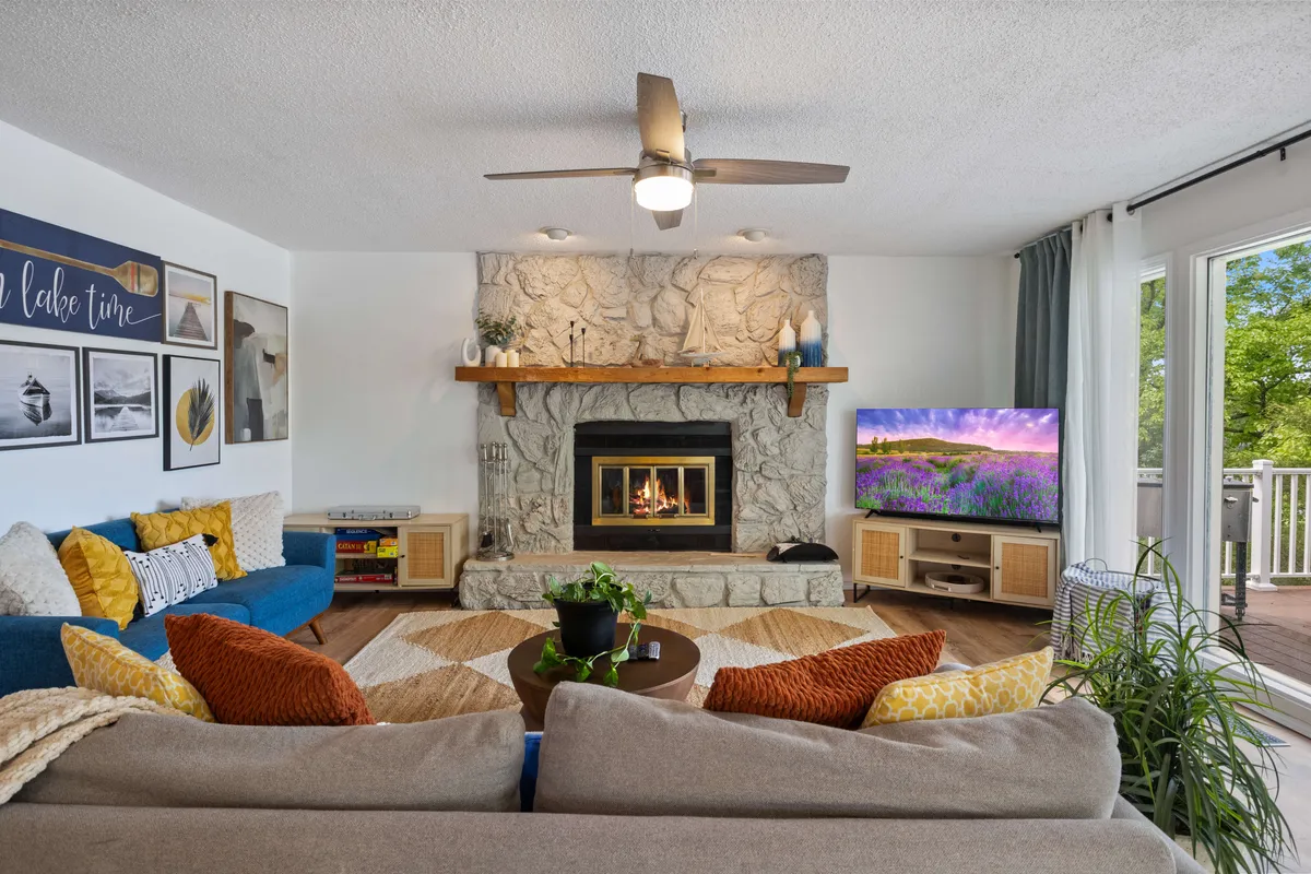 A comfortable living room with a fireplace, arranged sofas, a wall-mounted television, and decorative artwork. Large windows allow plenty of daylight to enter, creating a bright and relaxing atmosphere—ideal for both socializing and unwinding. The space feels inviting and perfect for movie nights or quiet conversations.
