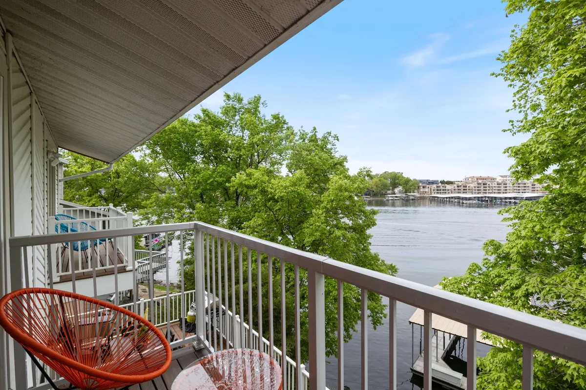 A balcony with a comfortable orange chair overlooks calm waters, framed by lush trees. The setting is peaceful and relaxed, ideal for sipping coffee, reading, or simply taking in the changing scenery as the seasons pass.