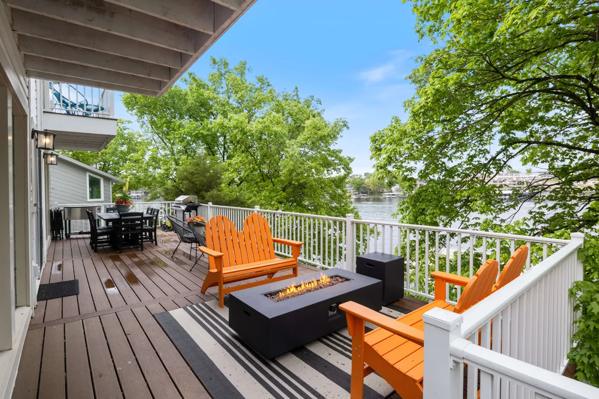 An inviting outdoor area with orange Adirondack chairs gathered around a fire pit, set against a scenic river view and green trees. The scene evokes cozy evenings of storytelling, roasting marshmallows, or enjoying sunsets as a family.