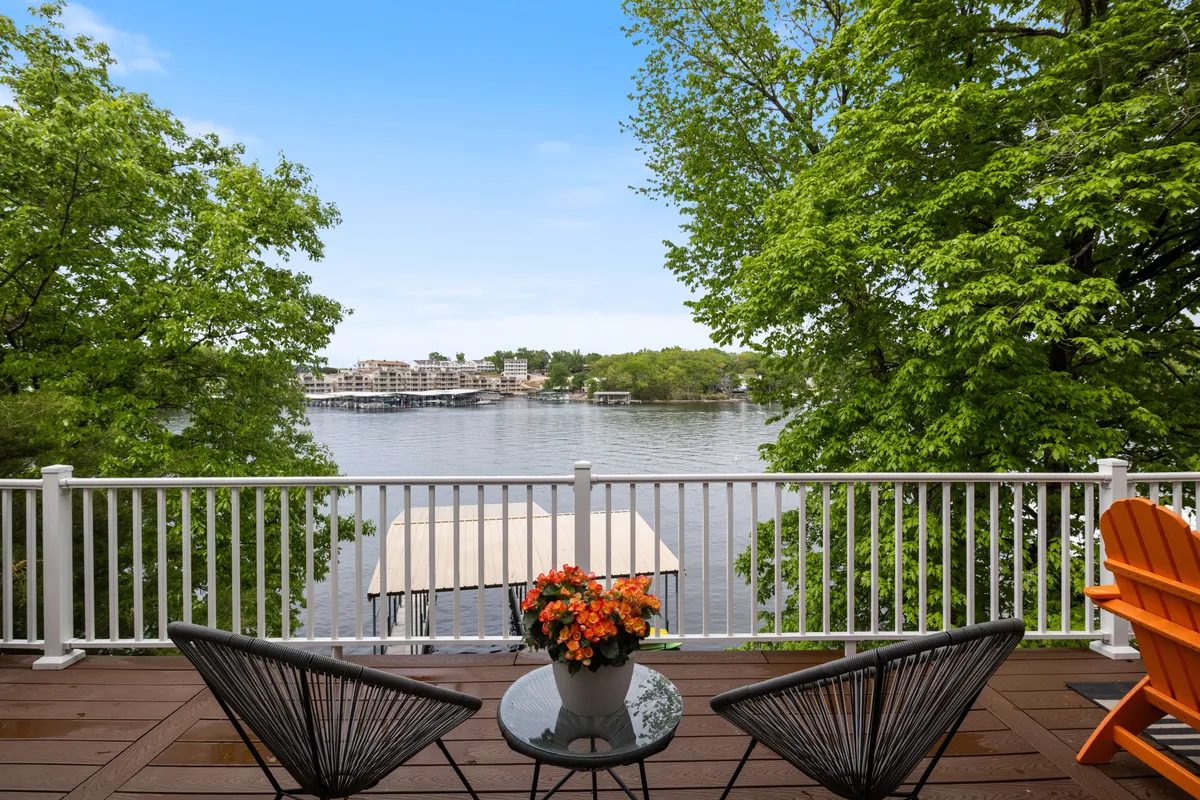 A serene deck overlooking the lake, furnished with comfortable seating and surrounded by potted flowers. The view is tranquil, ideal for morning coffee, socializing, or simply soaking up the scenery.